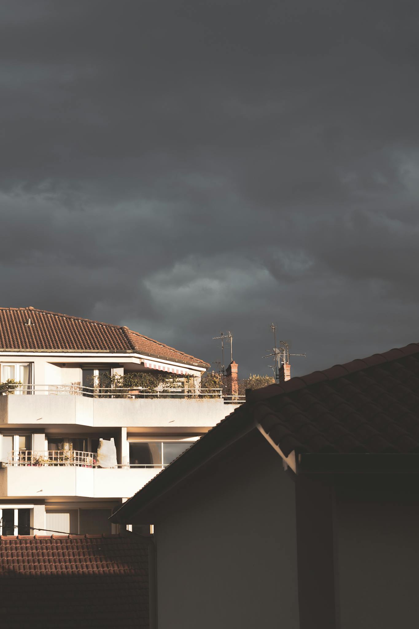 A moody evening sky with dark clouds over residential rooftops, creating a dramatic scene.